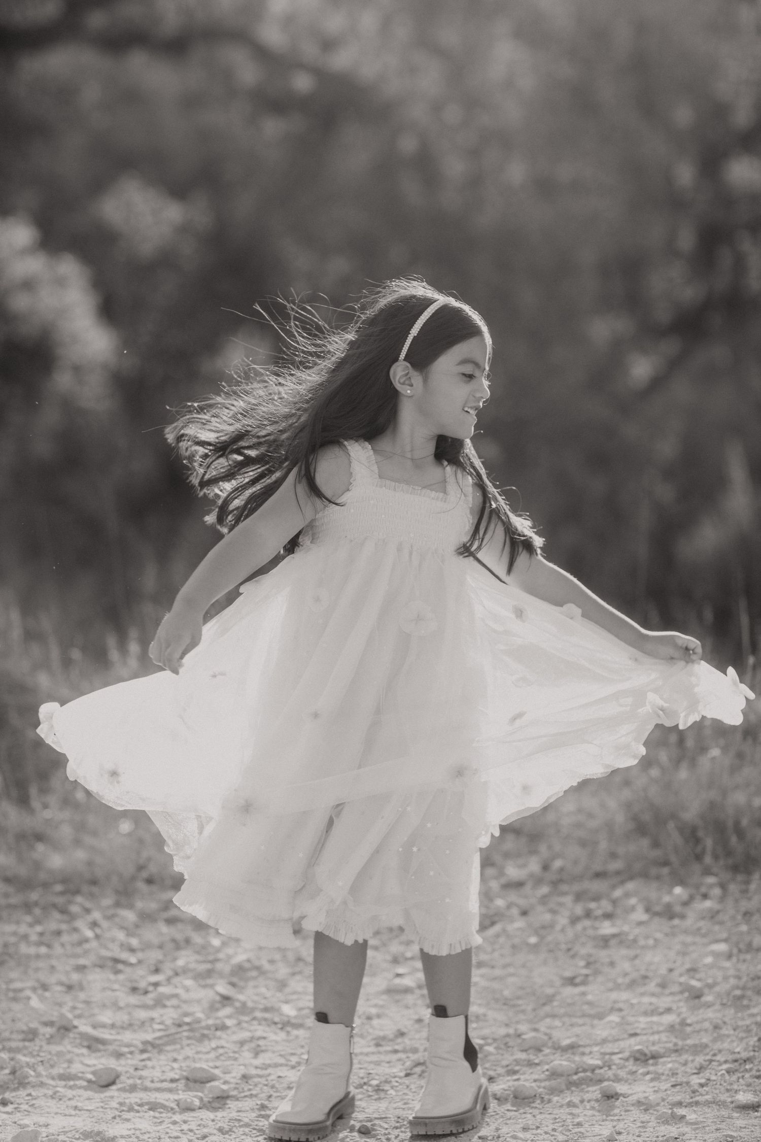 Black and white portrait of young girl twirling in white dress and boots outdoors.
