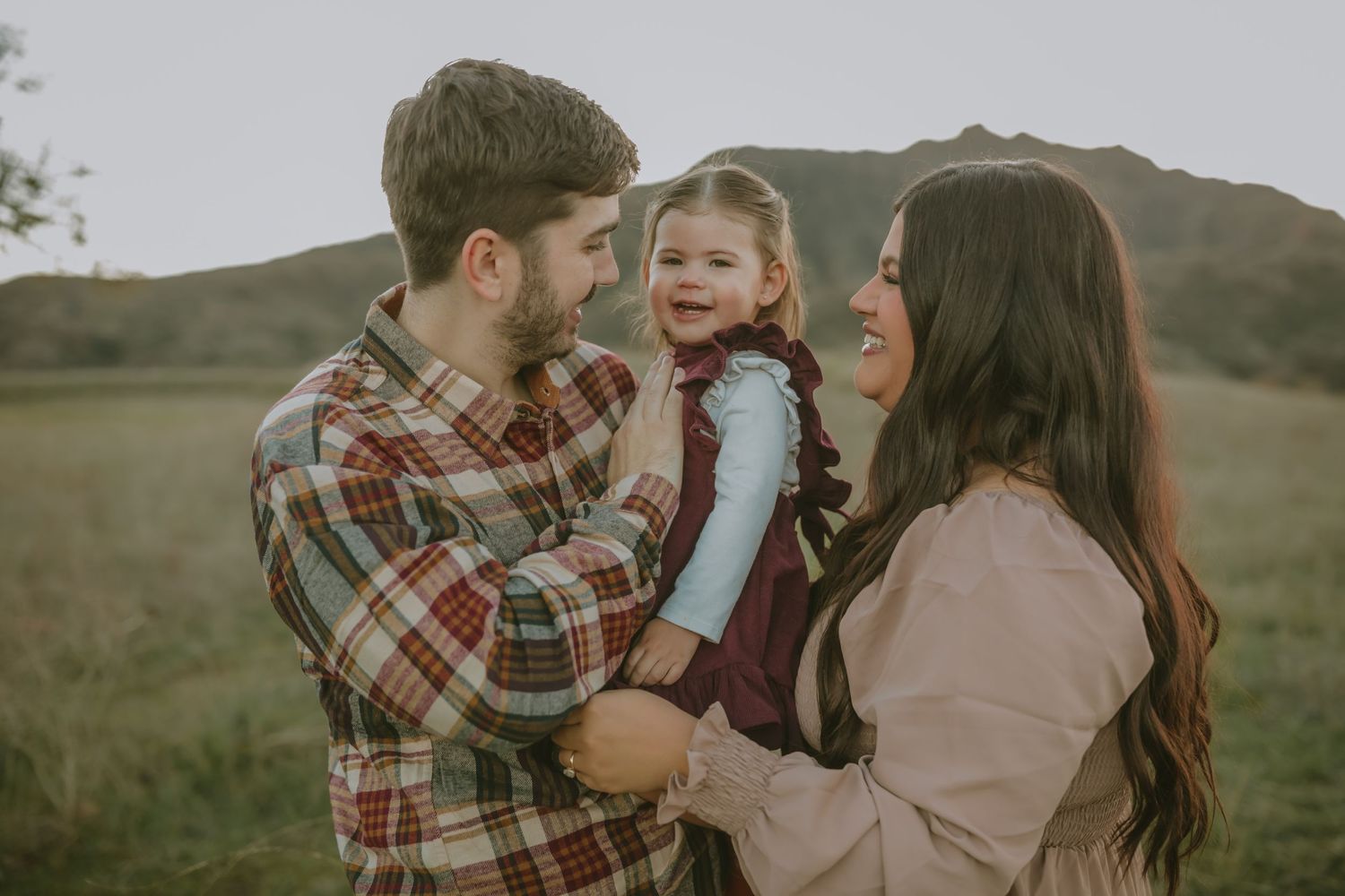 Family sharing laughs together in mountain field at dusk.