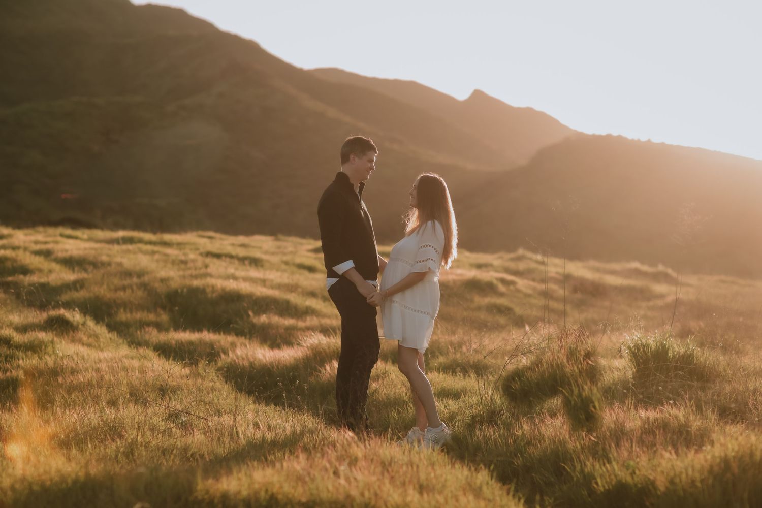 Couple standing together on hillside during golden hour.