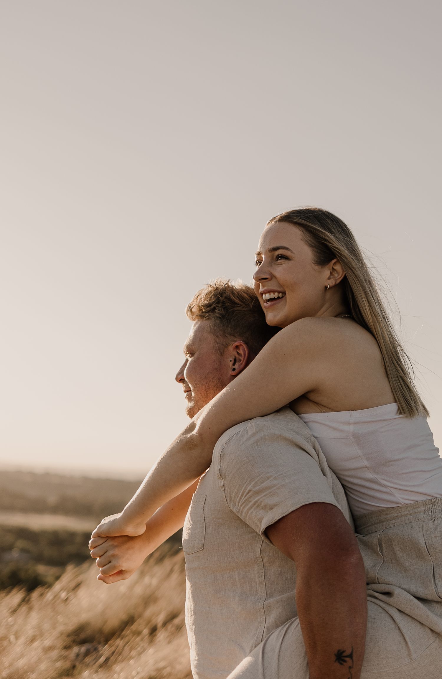 A joyful couple embraces in warm sunlight on a hilltop.