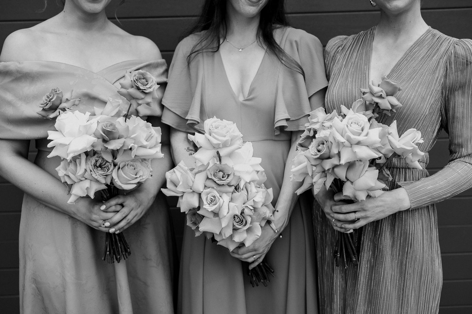 Three bridesmaids in pastel dresses holding floral bouquets in black and white.