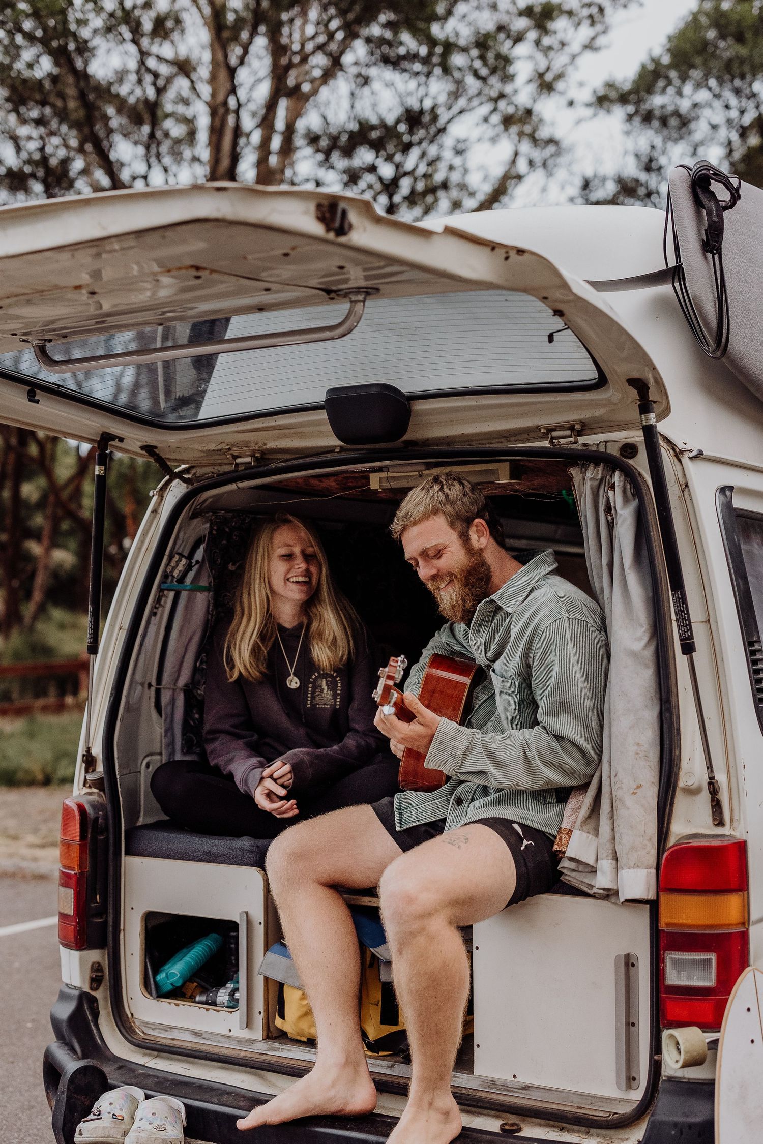 A couple sits in the back of a white van, sharing music with an acoustic guitar.