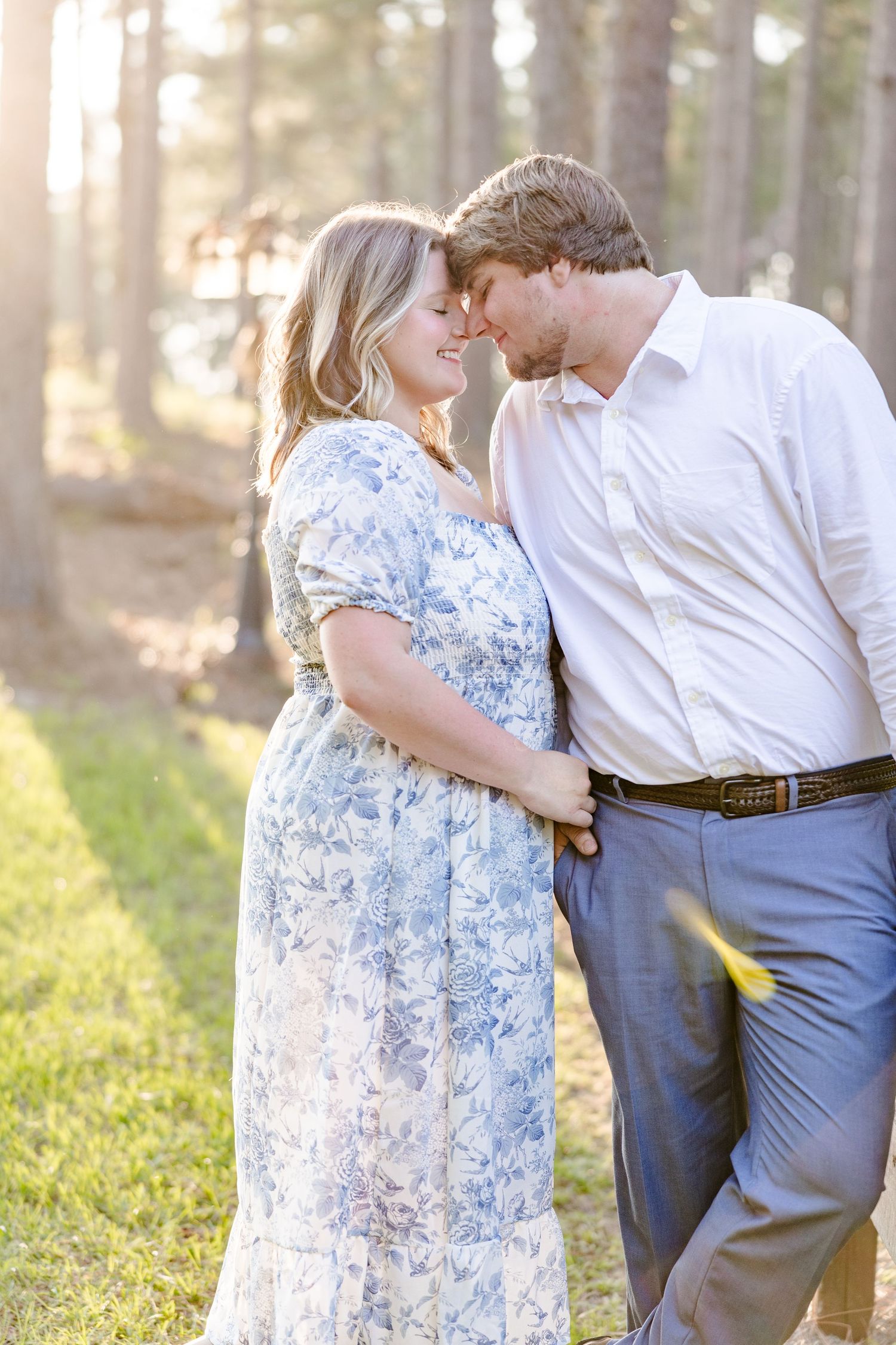 A romantic outdoor portrait of a couple embracing against a backdrop of tall pine trees.