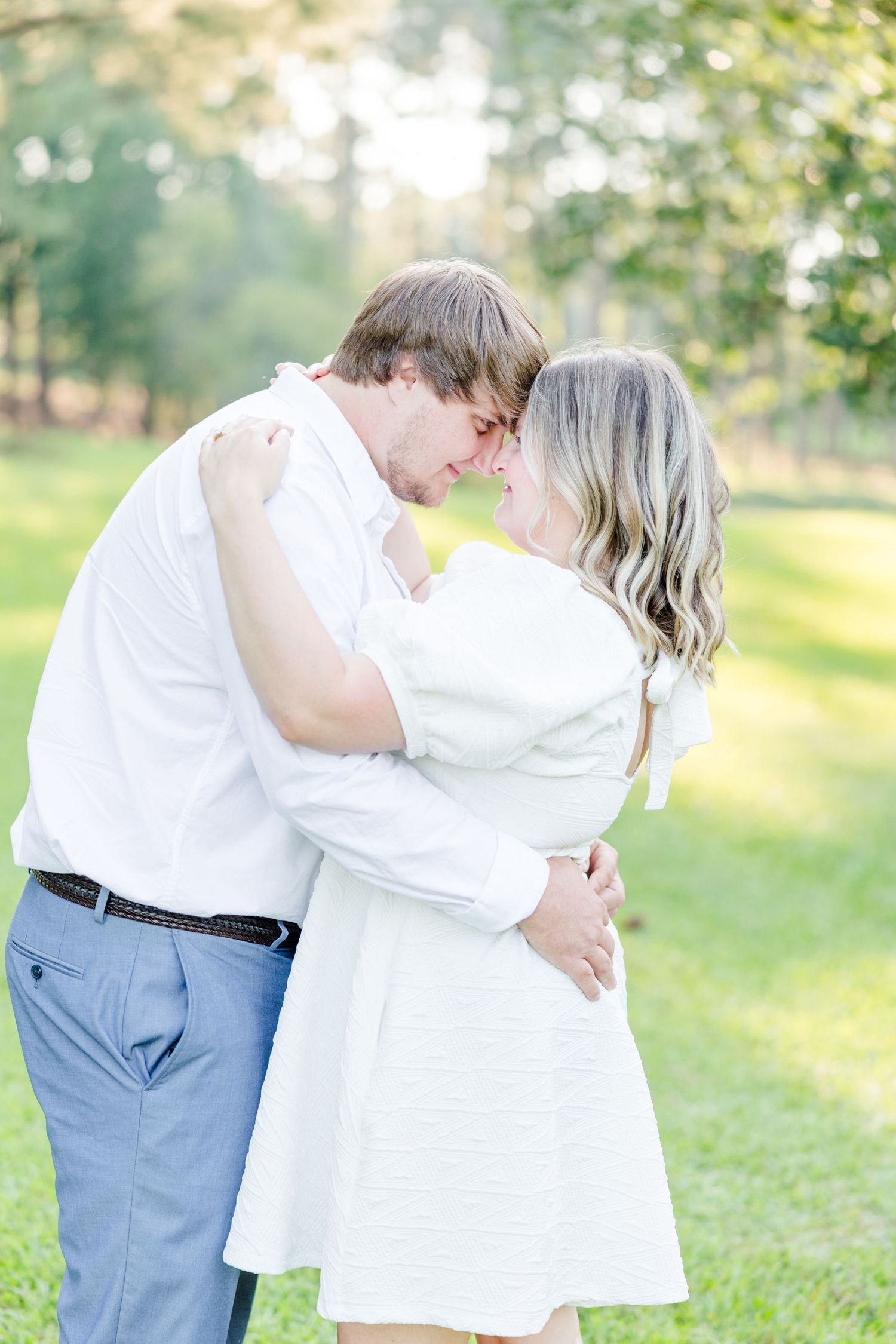 A couple shares intimate moments during their engagement photos in a sunny outdoor setting.