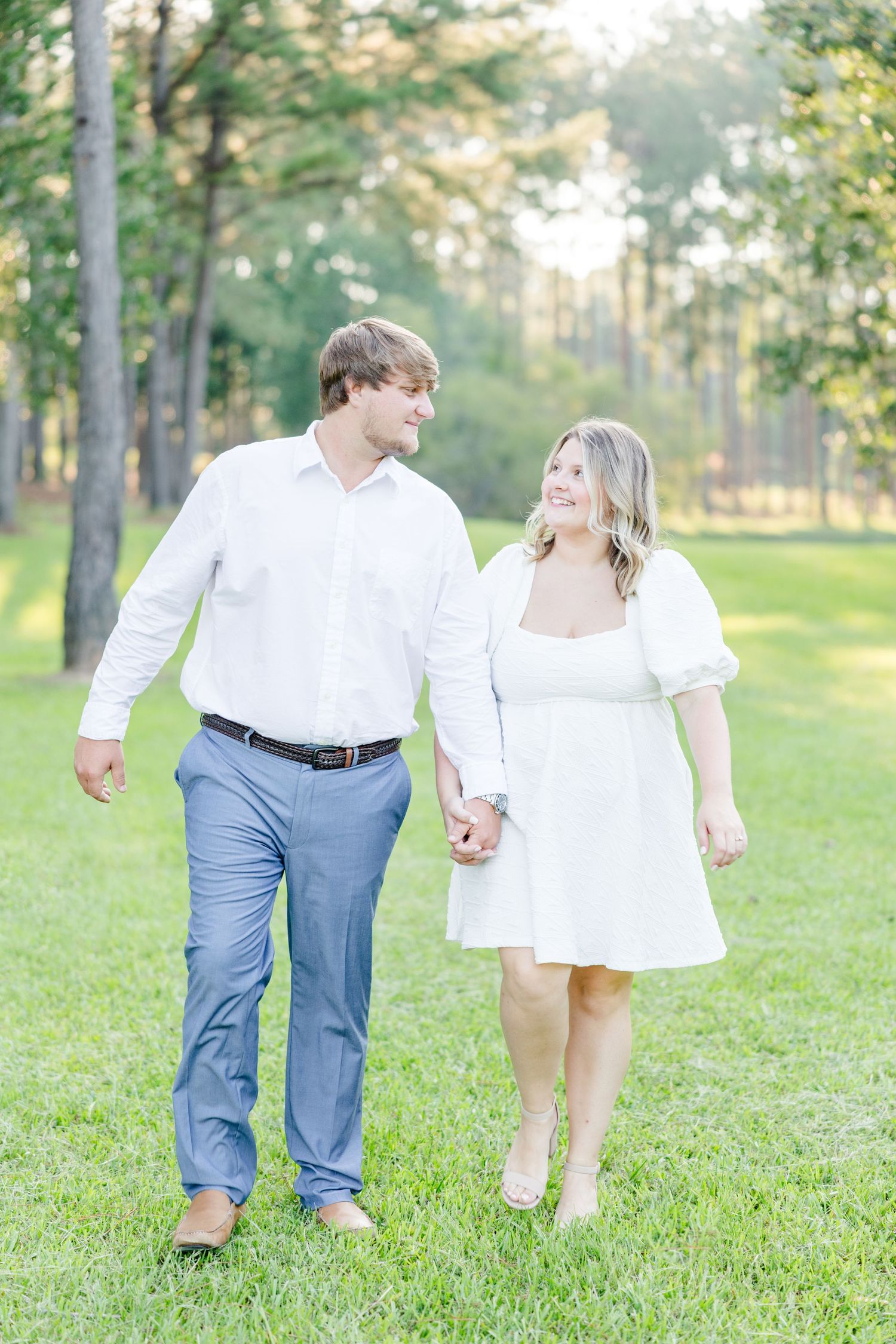 Couple walks hand in hand through a sunlit park during their engagement photo session.
