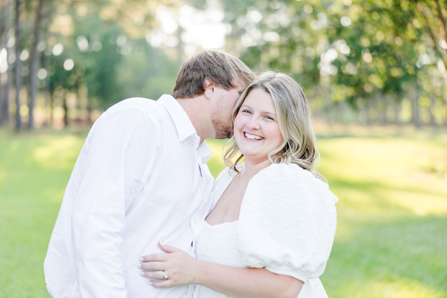 Sweet candid moments between a couple dressed in white during their engagement photoshoot in a park.