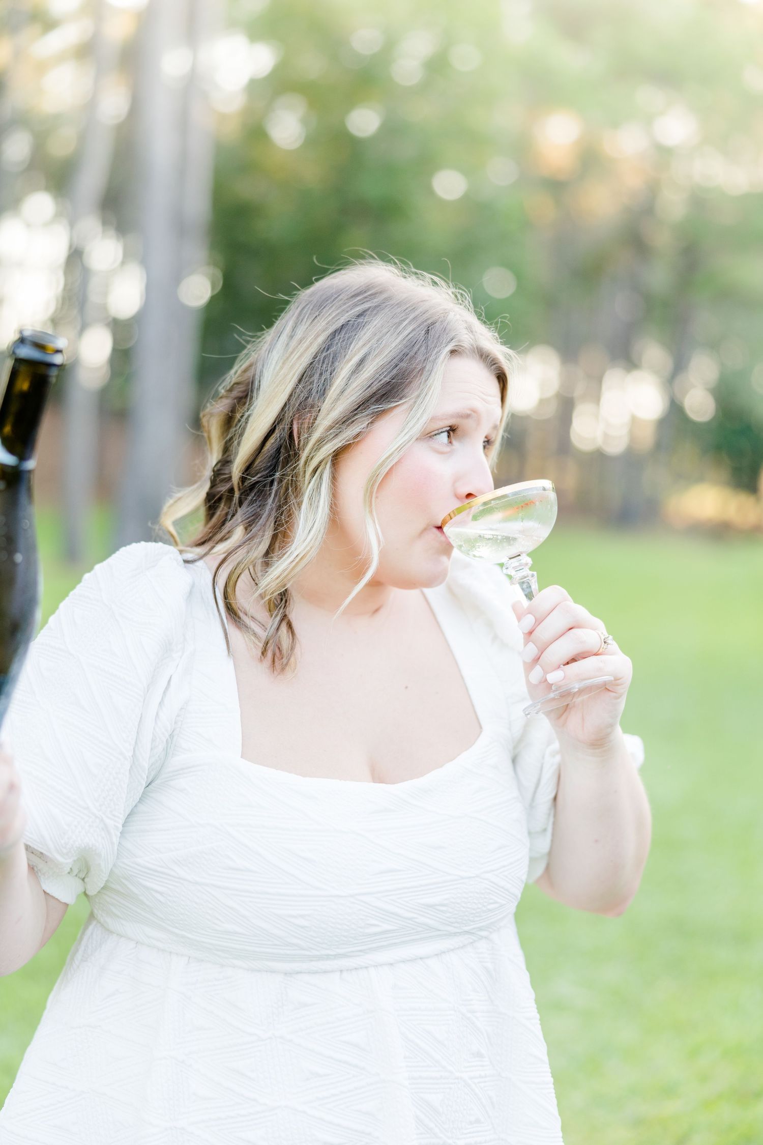 Person in white dress enjoying champagne in an ethereal outdoor setting.