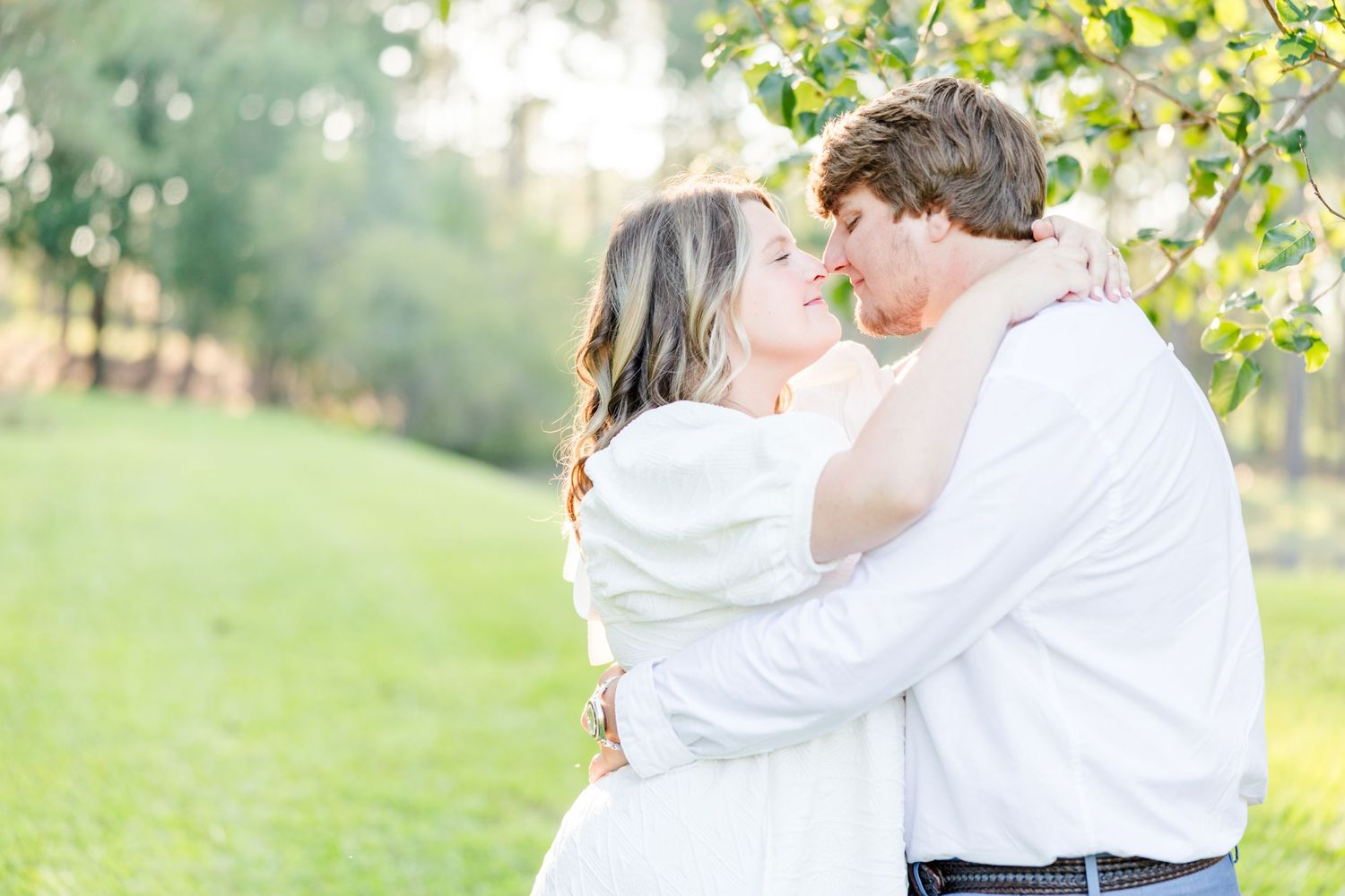 Romantic couple embracing in a sunlit garden setting wearing white and blue outfits.