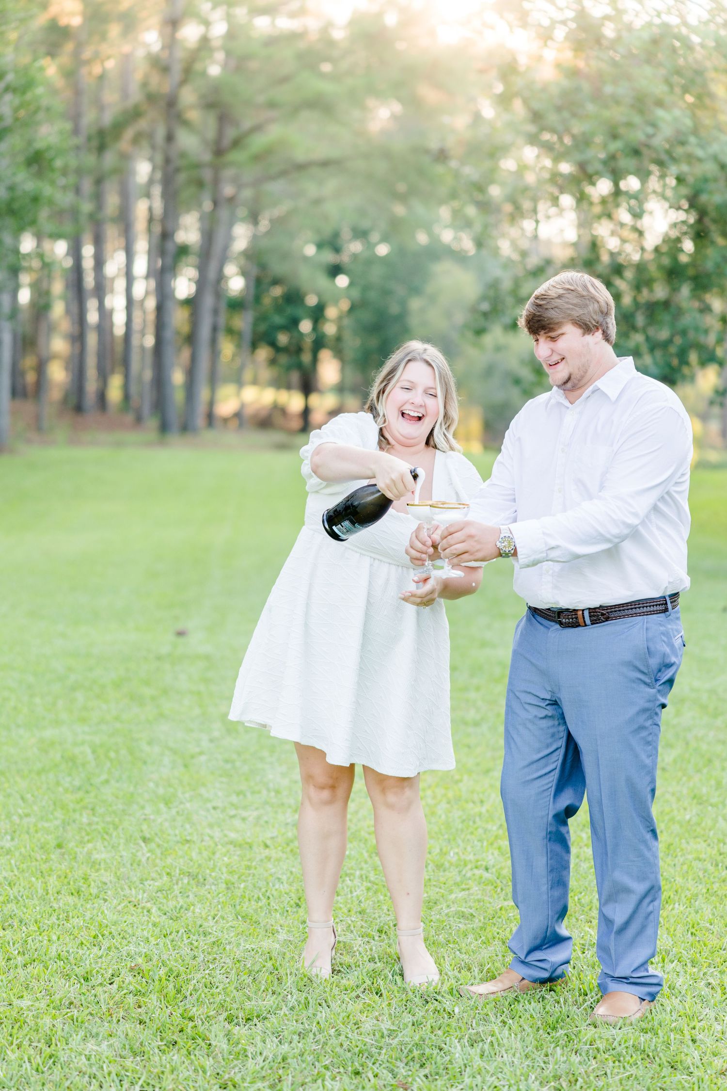 Couple enjoying a champagne celebration photoshoot in a sunlit park setting.