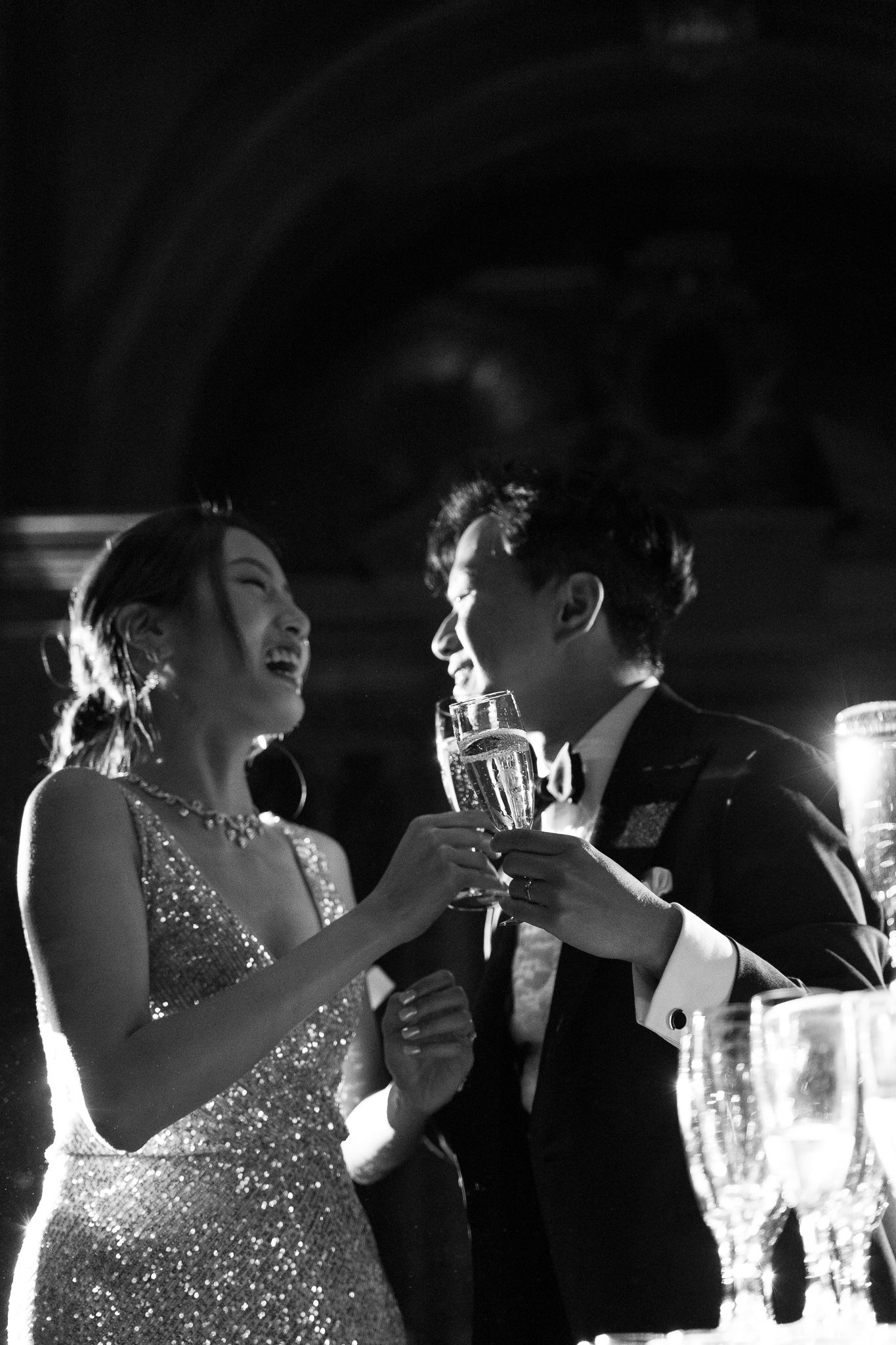 A couple shares a dance at a reception with the person in a sparkling dress glowing under dramatic lighting.