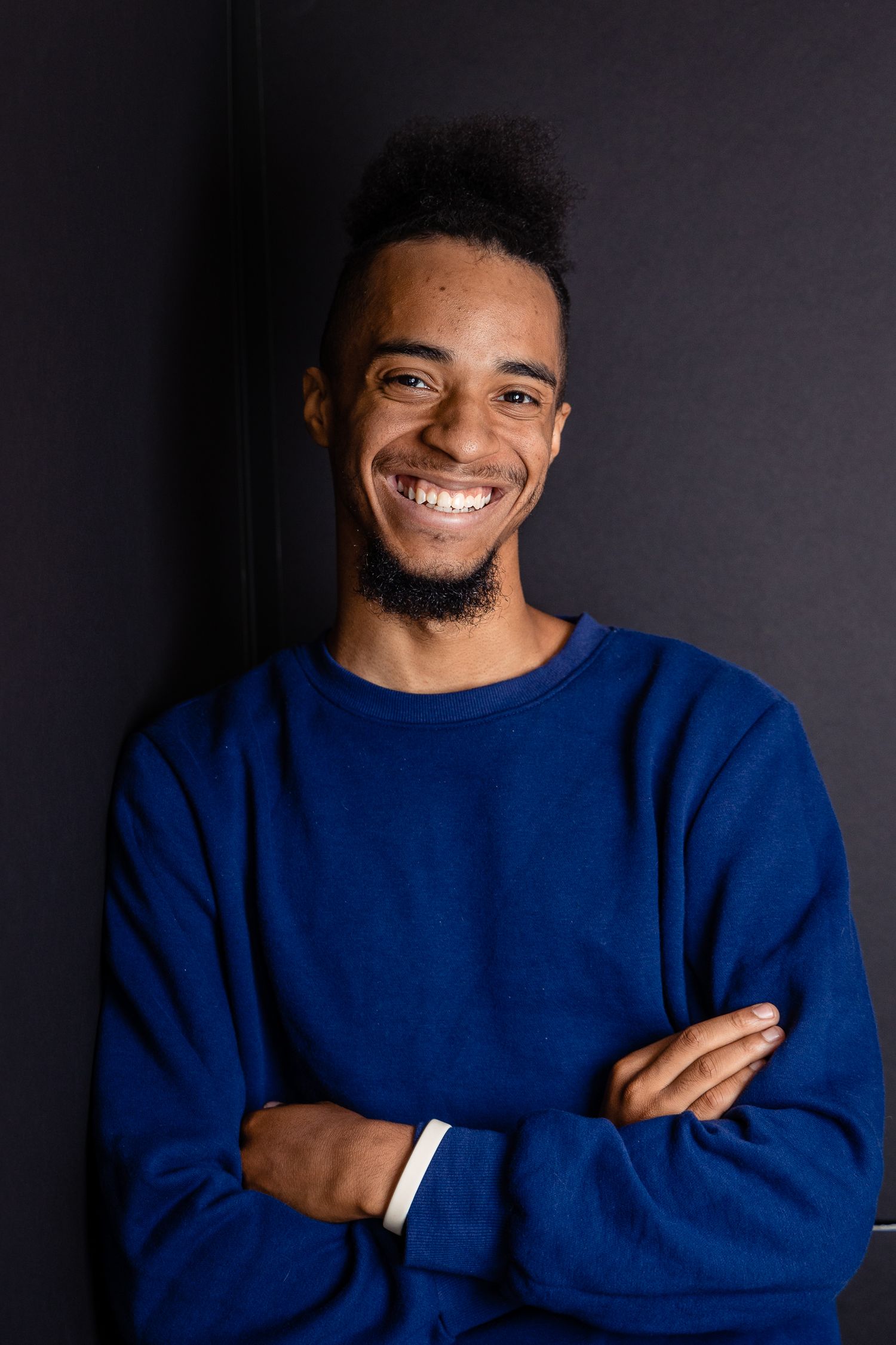 Portrait of a person in a blue sweater smiling against a dark background.