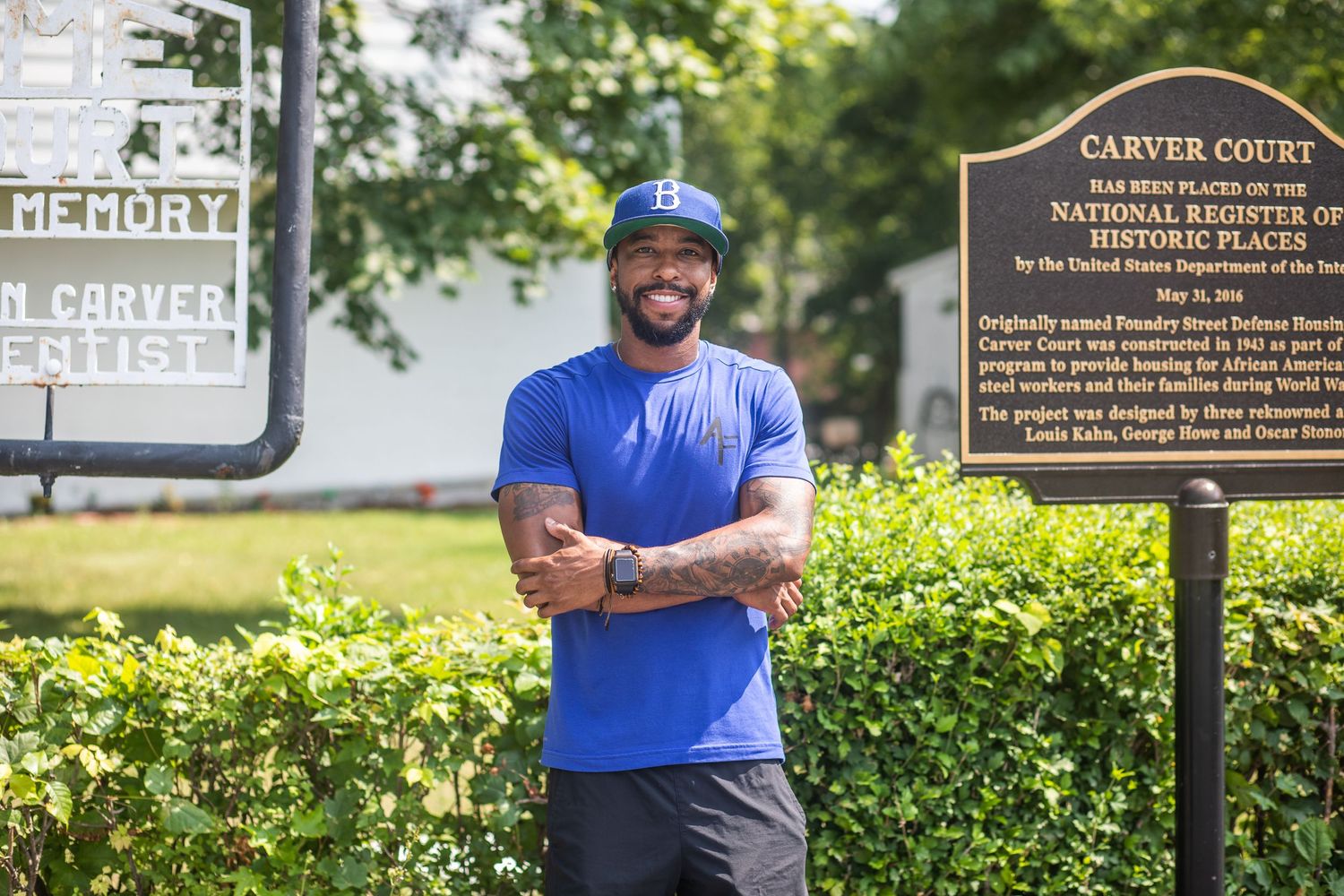 Athletic person in blue t-shirt poses with crossed arms near historical marker sign.