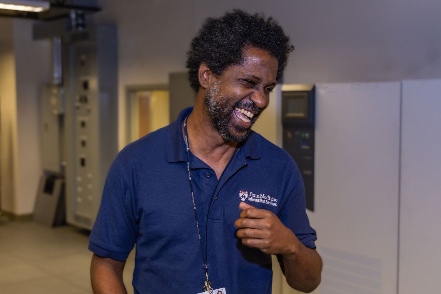 Person in a navy polo shirt laughing in an office hallway.