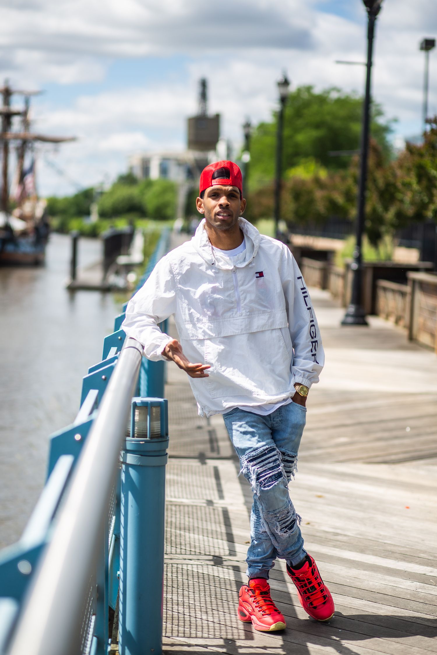 Person in white shirt and red cap leaning on railing along waterfront boardwalk.