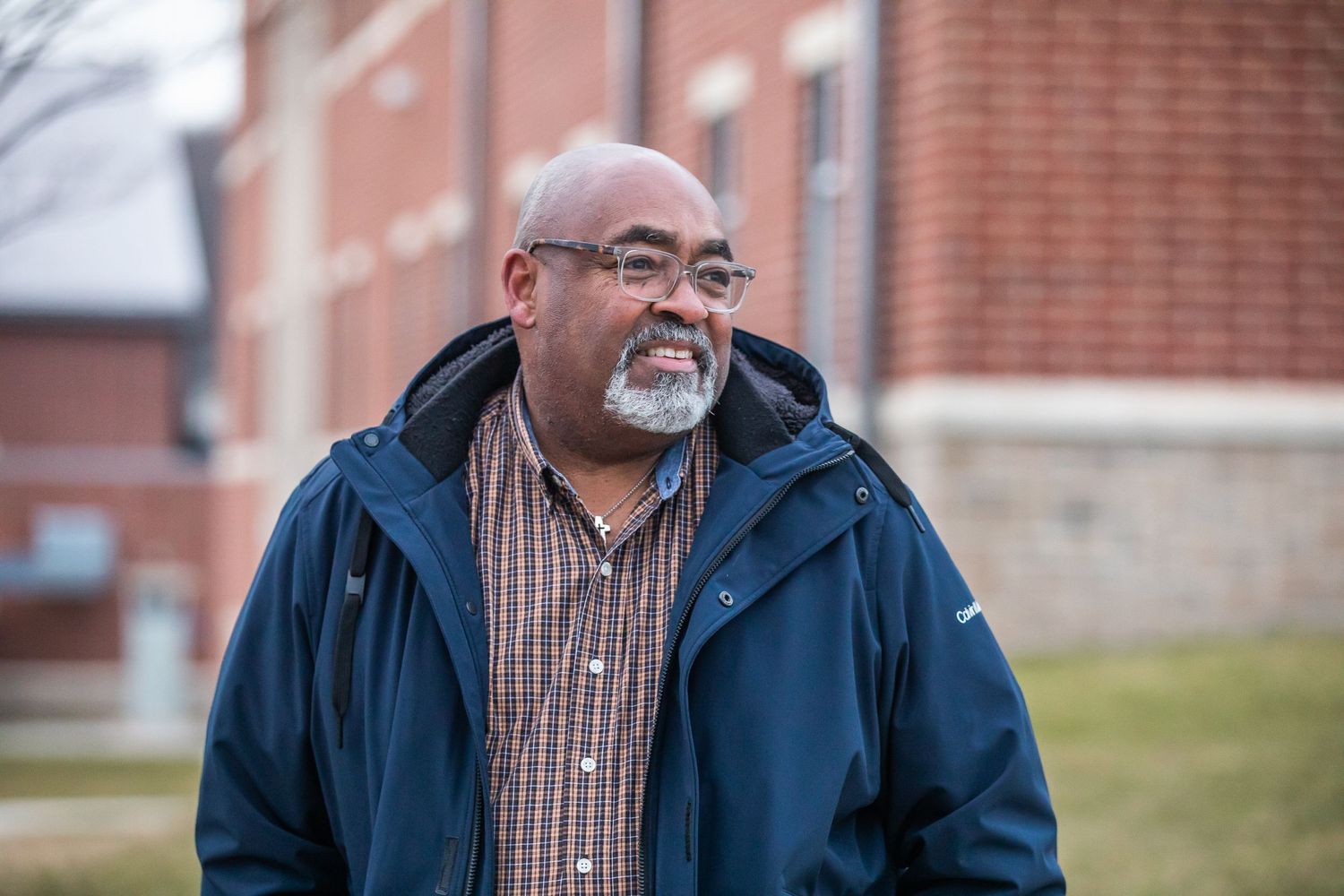 Person wearing blue jacket and plaid shirt standing outside brick building.