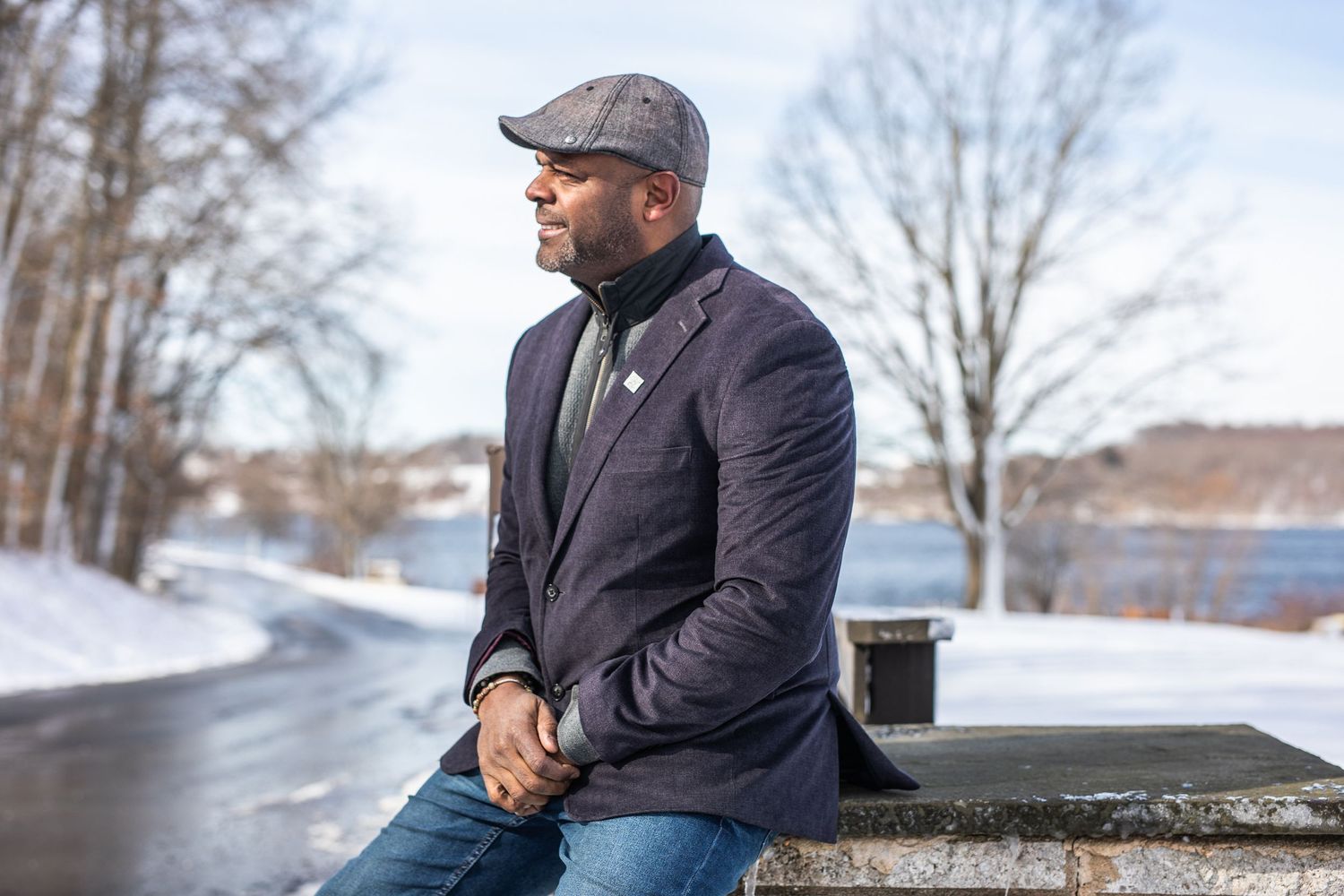 Person in winter clothing sitting on stone wall by snowy path.