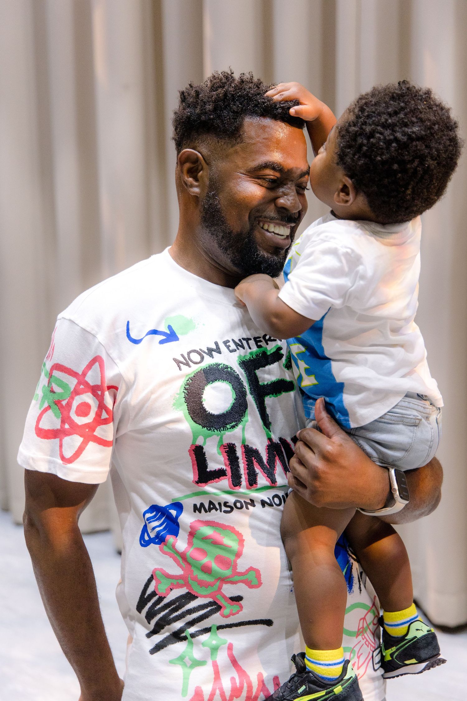 Parent and toddler share joyful moment while wearing casual attire with colorful graphic t-shirt.