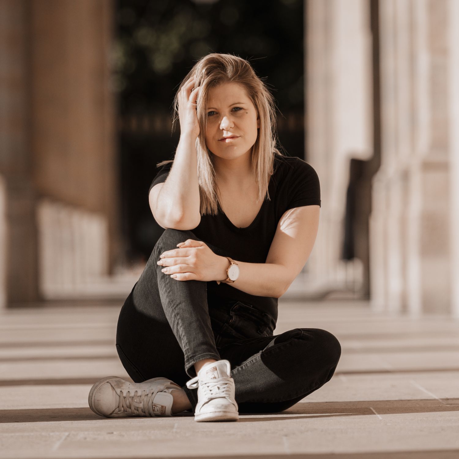Person in black outfit sits cross-legged on floor beside architectural columns.