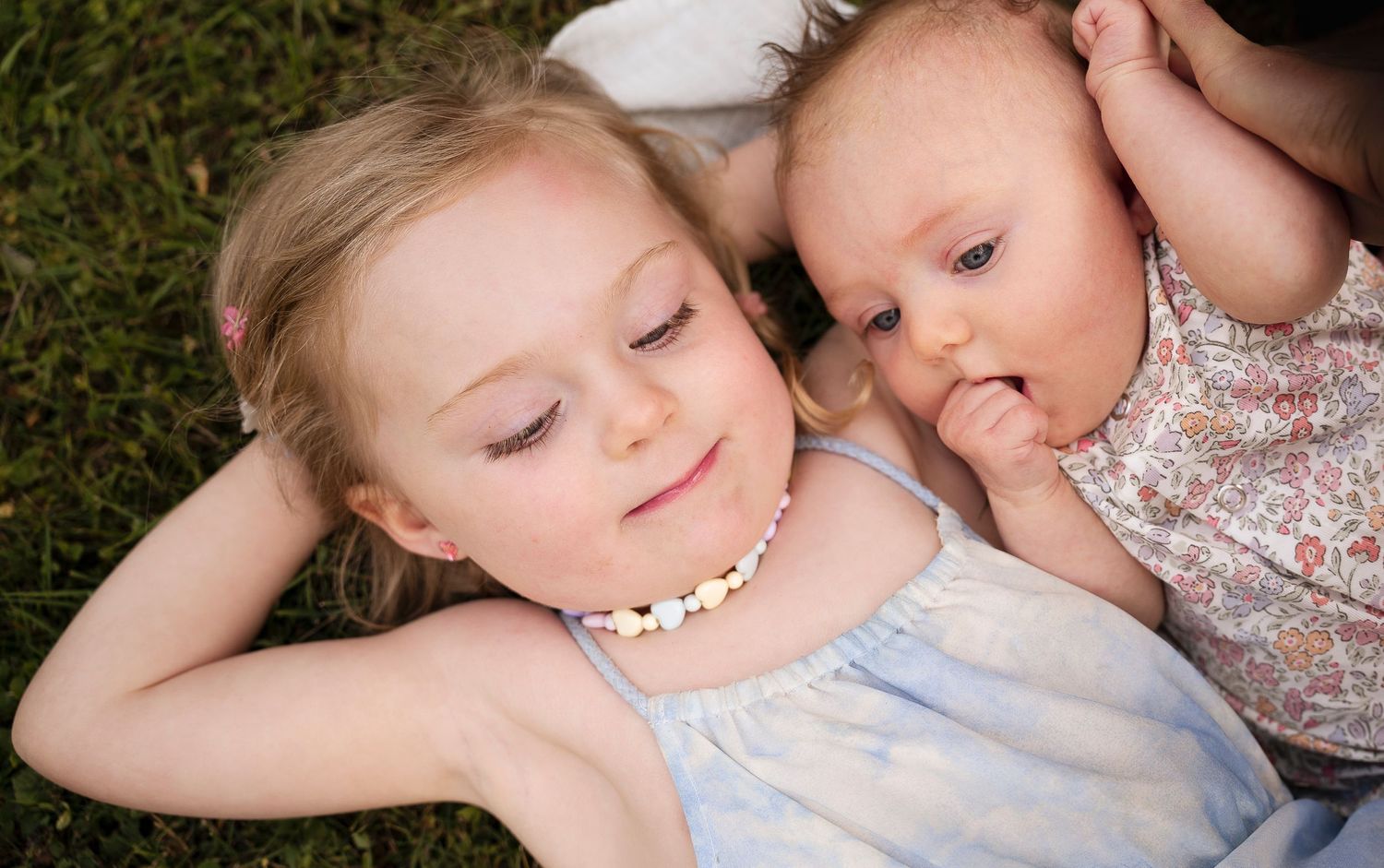 Sweet moment of closeness between siblings wearing summer outfits and laying on grass.