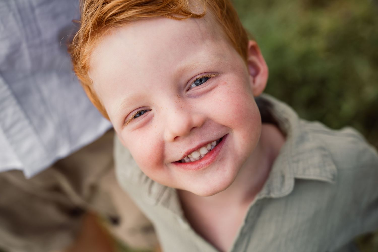 A bright-eyed youth with vibrant red hair smiles warmly at the camera in a casual portrait.