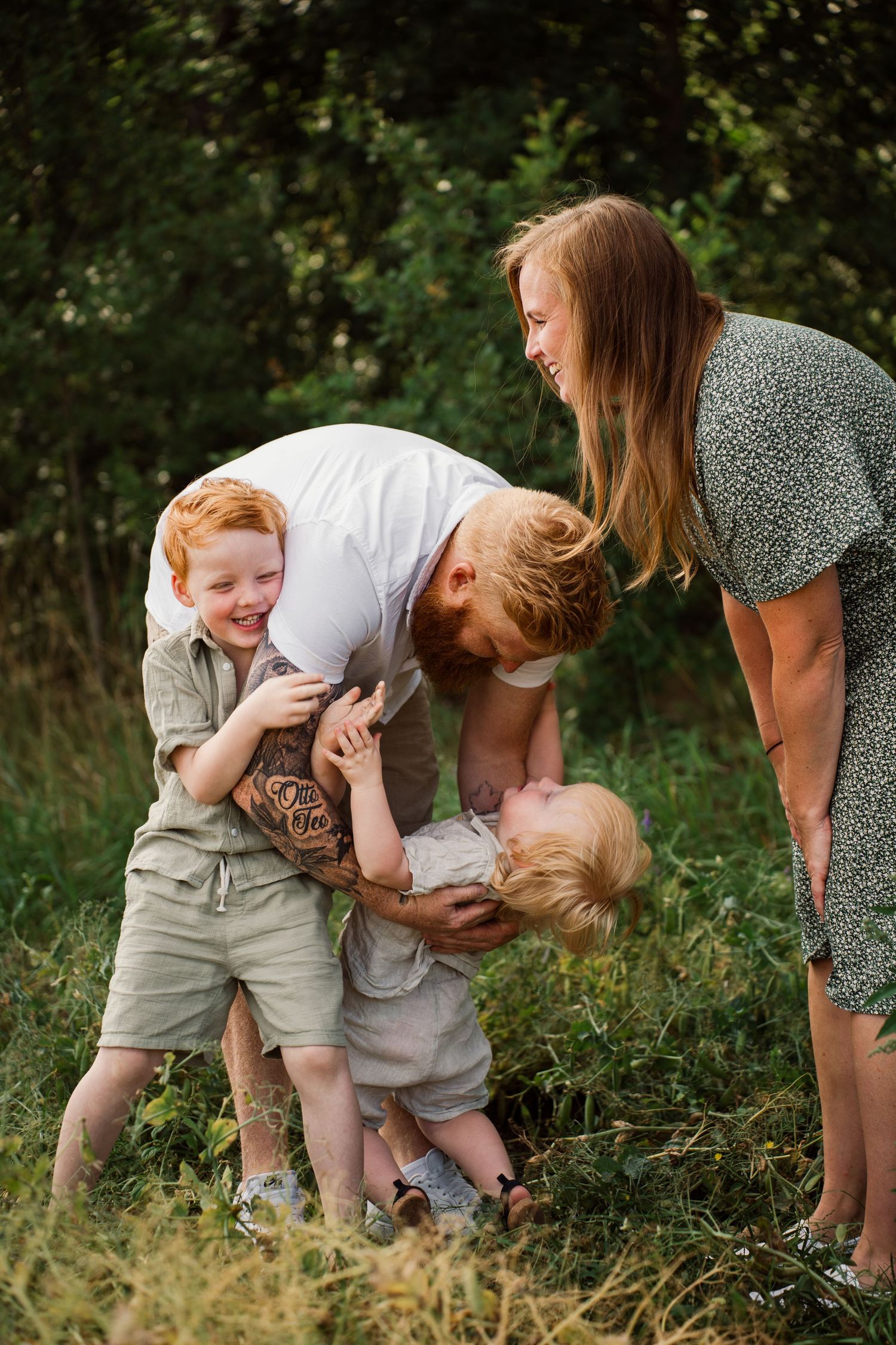 Playful family interaction in a sun-dappled grassy field during summer.