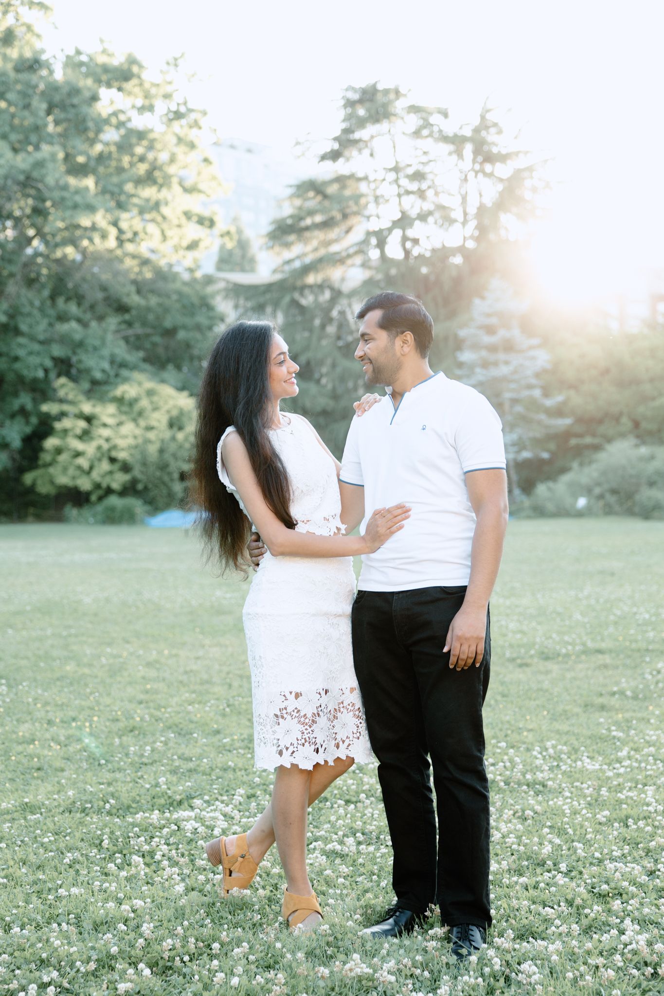 Couple shares a loving moment in white attire against a sunset garden backdrop.