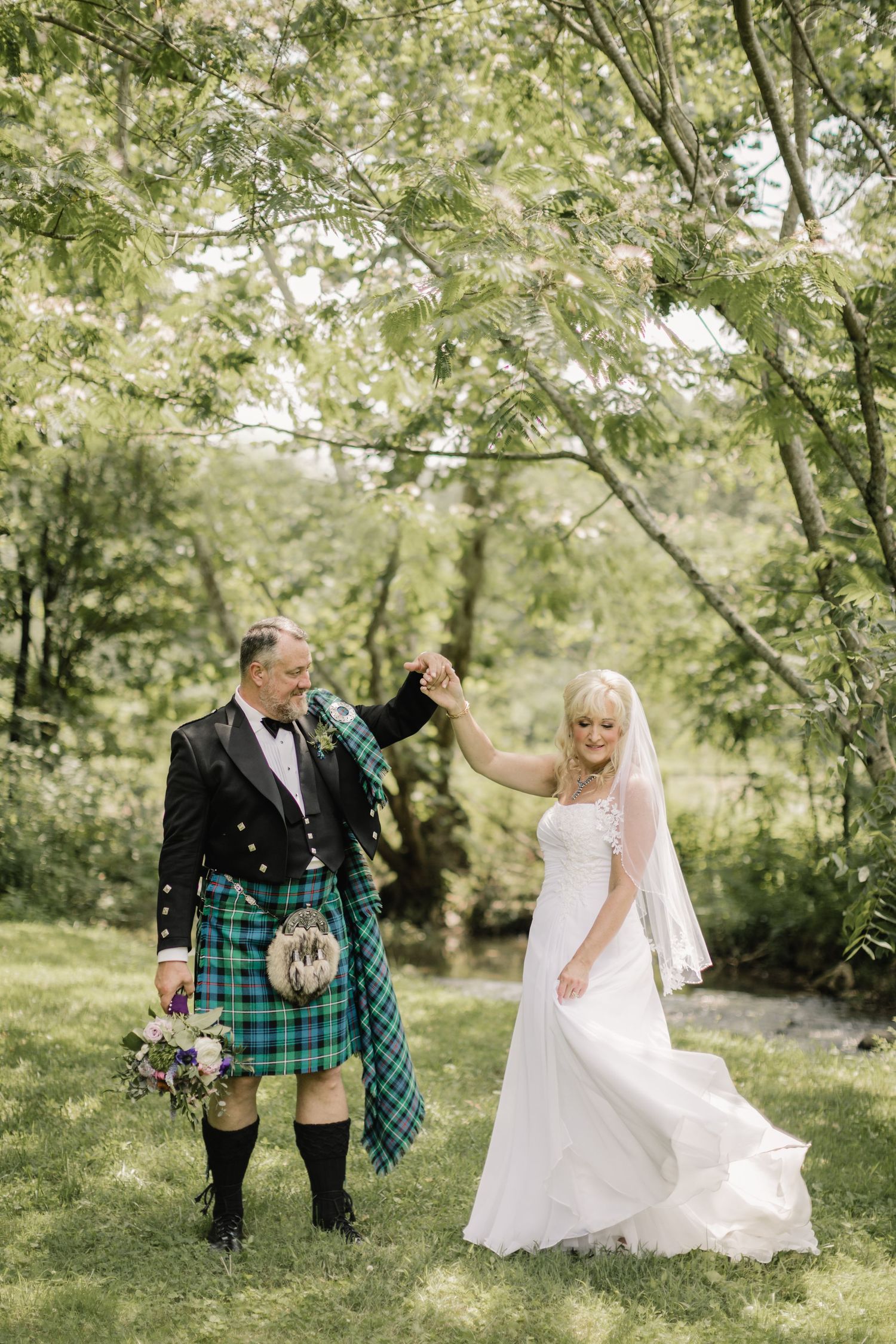 Scottish wedding couple dancing outdoors with bride in white and groom in traditional kilt.