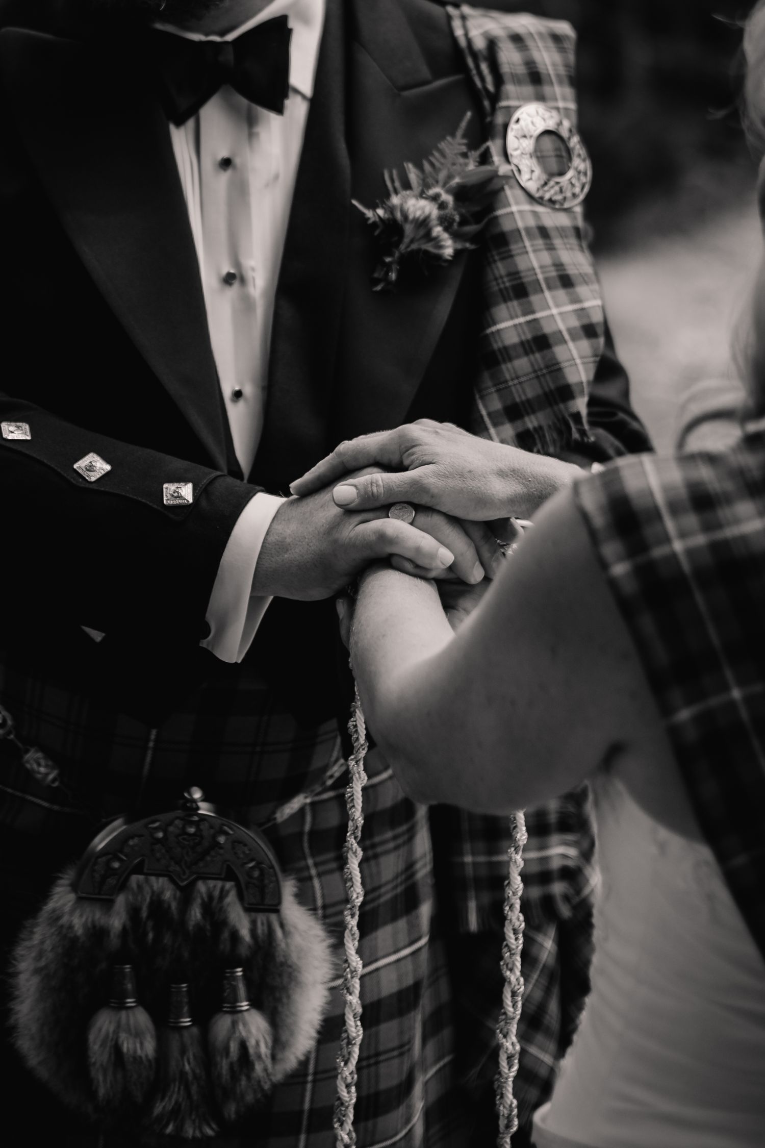 Black and white close-up of traditional Scottish wedding ceremony hands and kilt details.