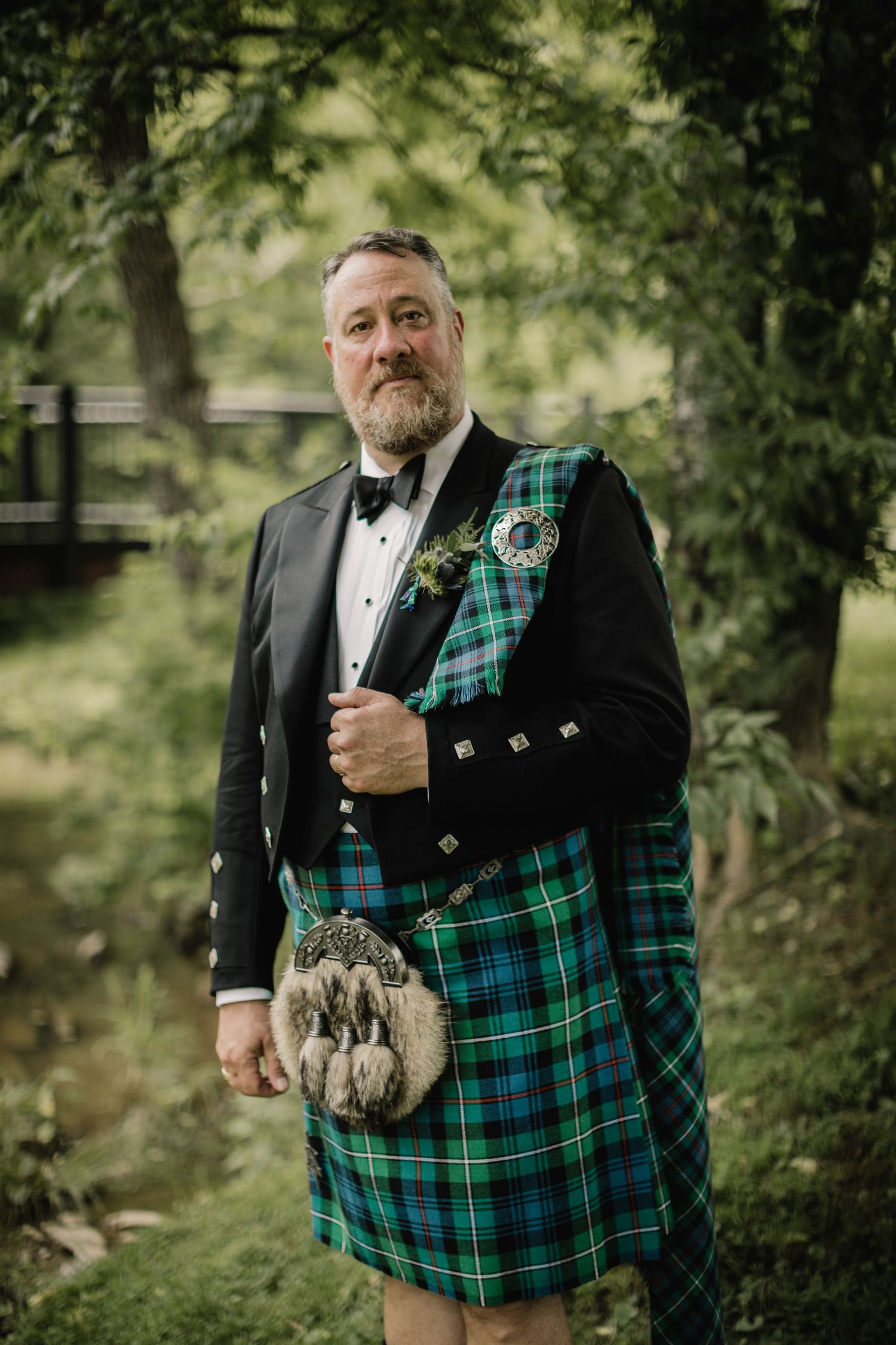 A traditional Scottish wedding outfit featuring a green and blue tartan kilt, sporran, and formal black jacket.