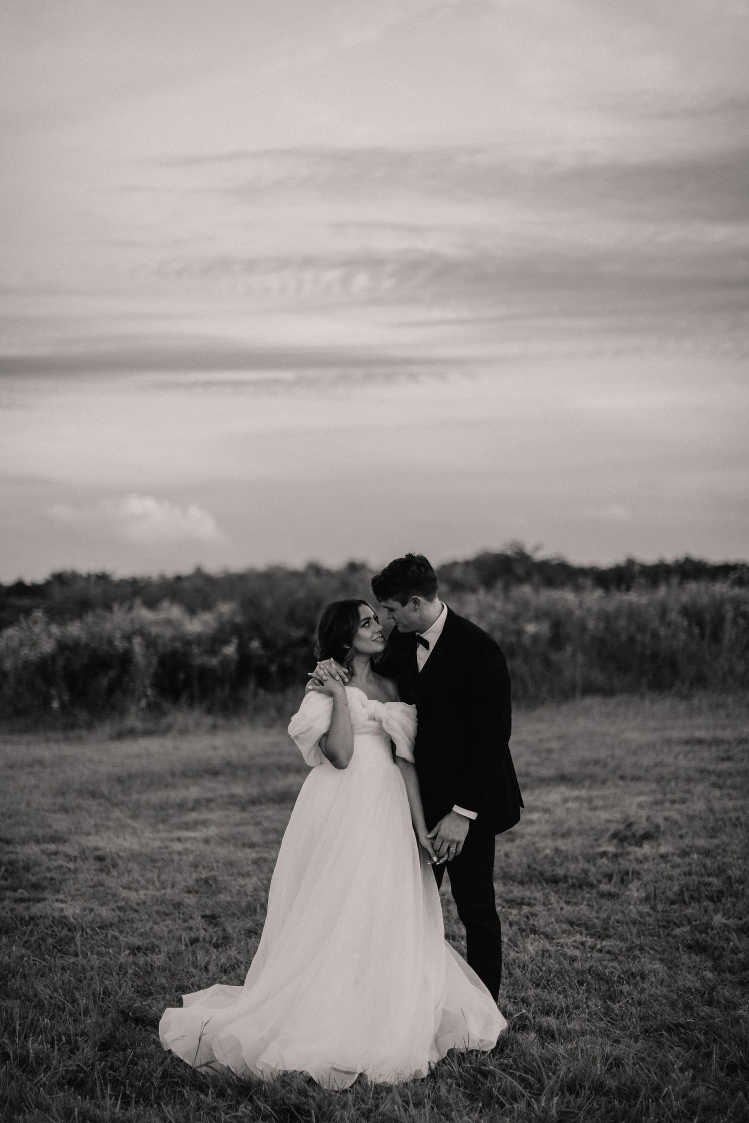 Classic black and white wedding portrait of couple in field under dramatic sky.