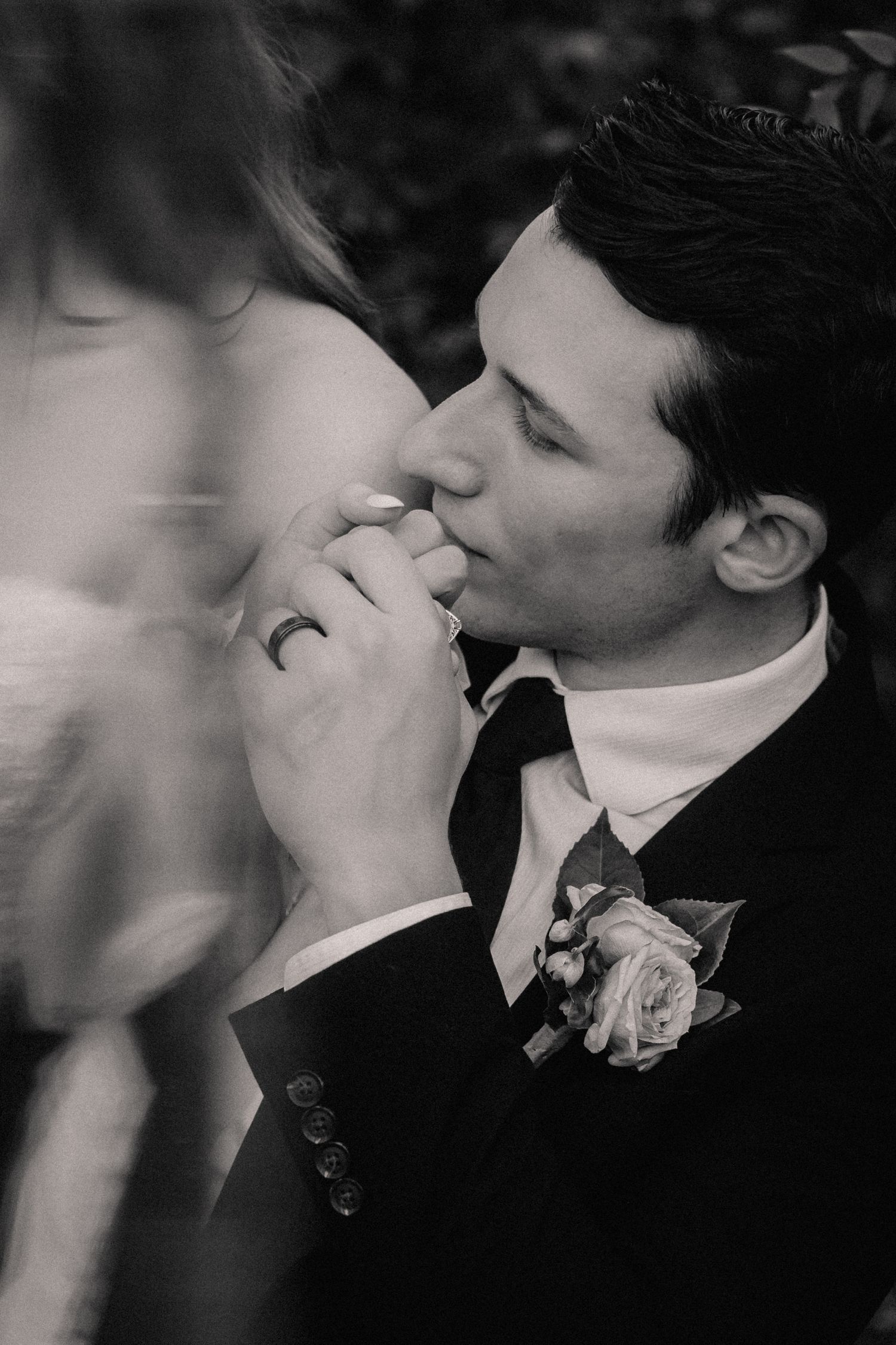 Intimate black and white wedding portrait capturing a tender moment with a boutonniere detail.