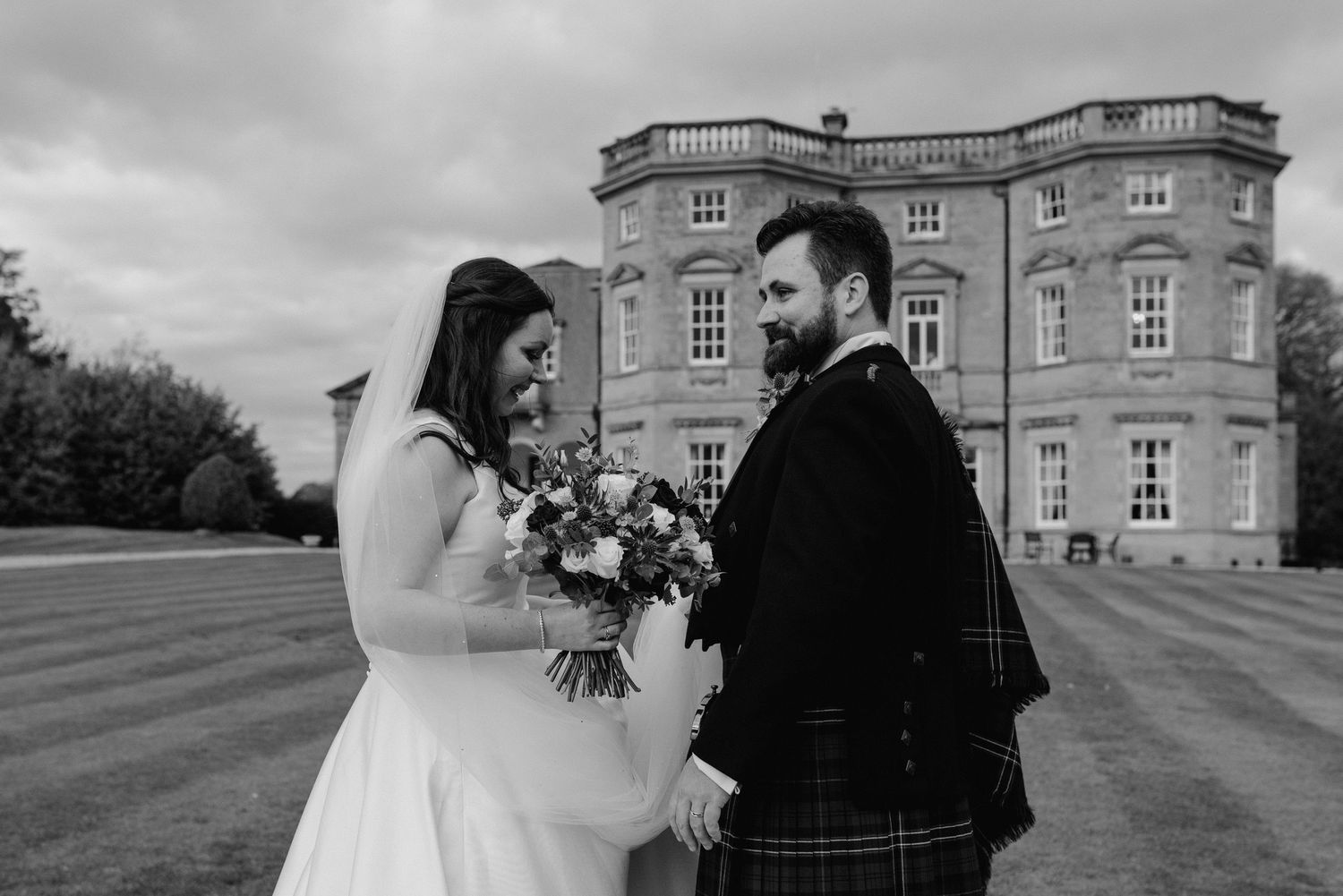 Black and white wedding photo of couple standing in front of a grand mansion.