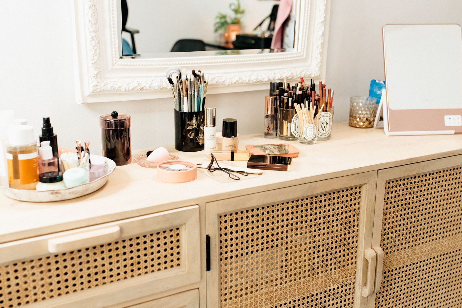 Elegant makeup vanity with cane cabinet doors displaying organized beauty products and brushes.