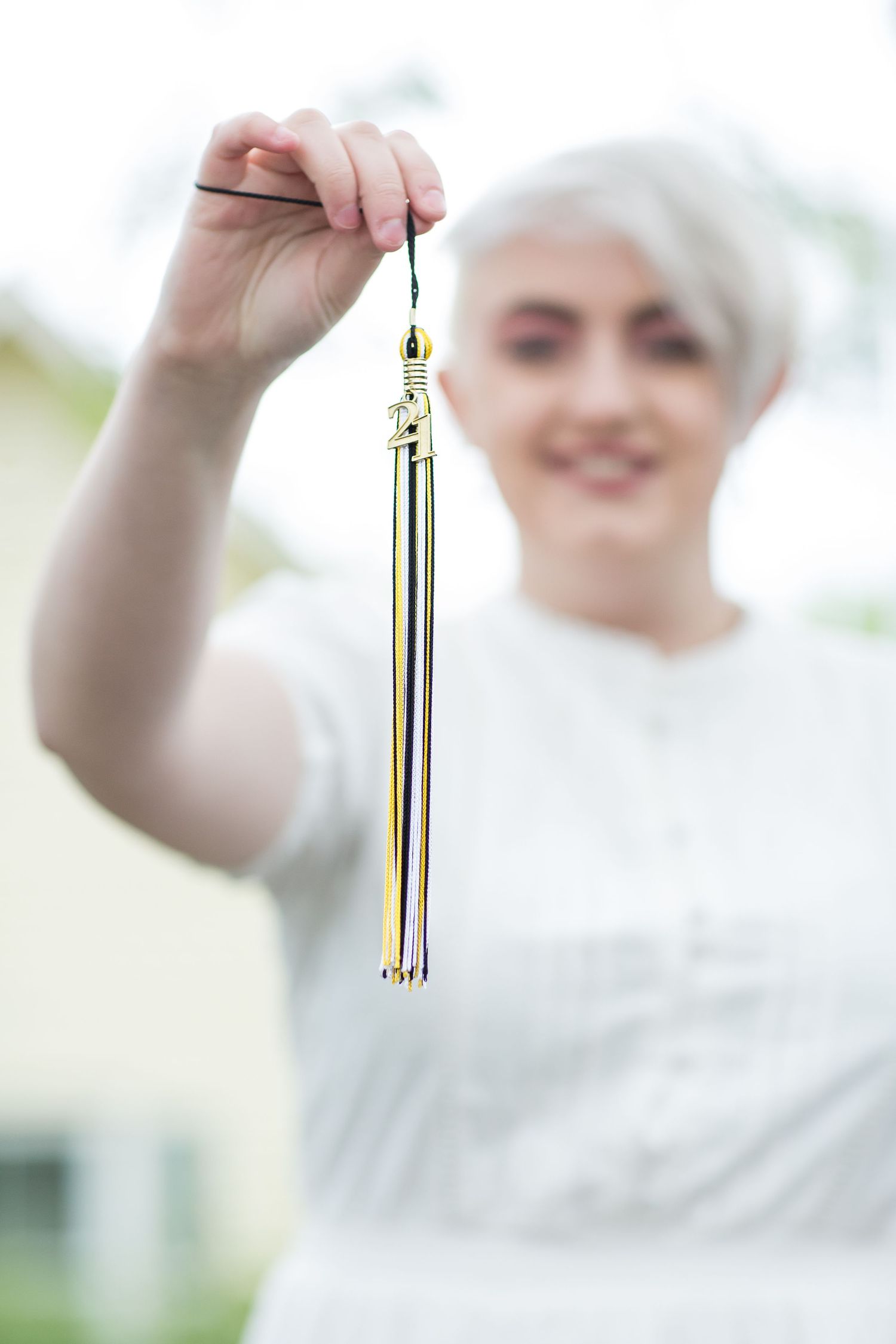 Smiling graduate holds gold tassel outdoors after graduation ceremony.