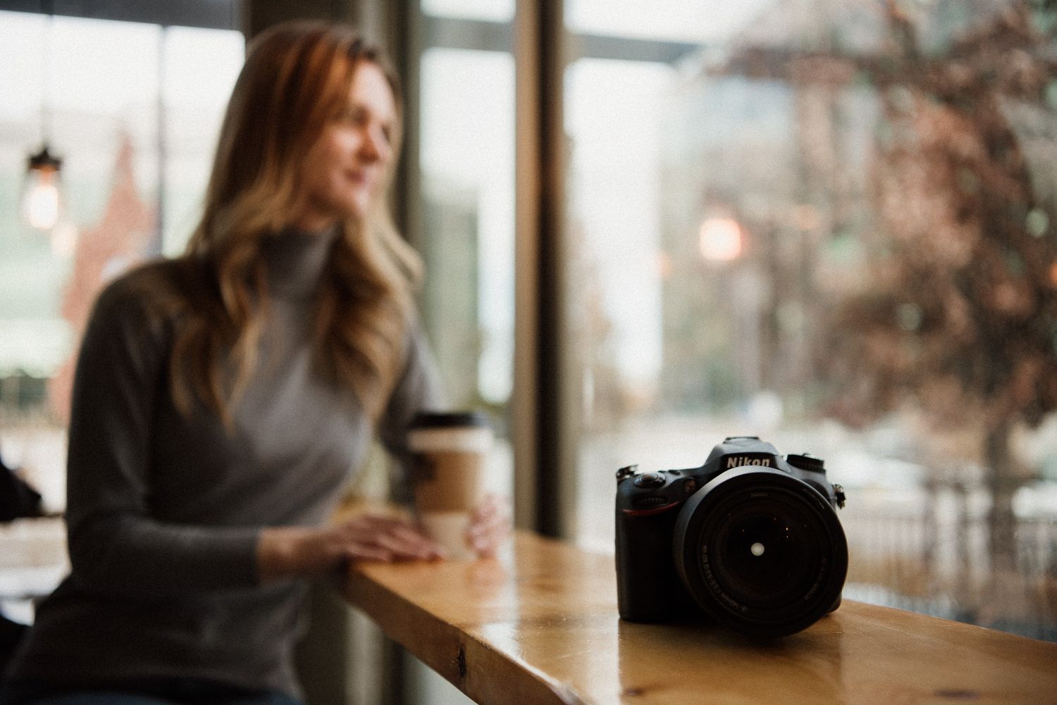 A professional camera sits on wooden table in a cafe with blurred background.