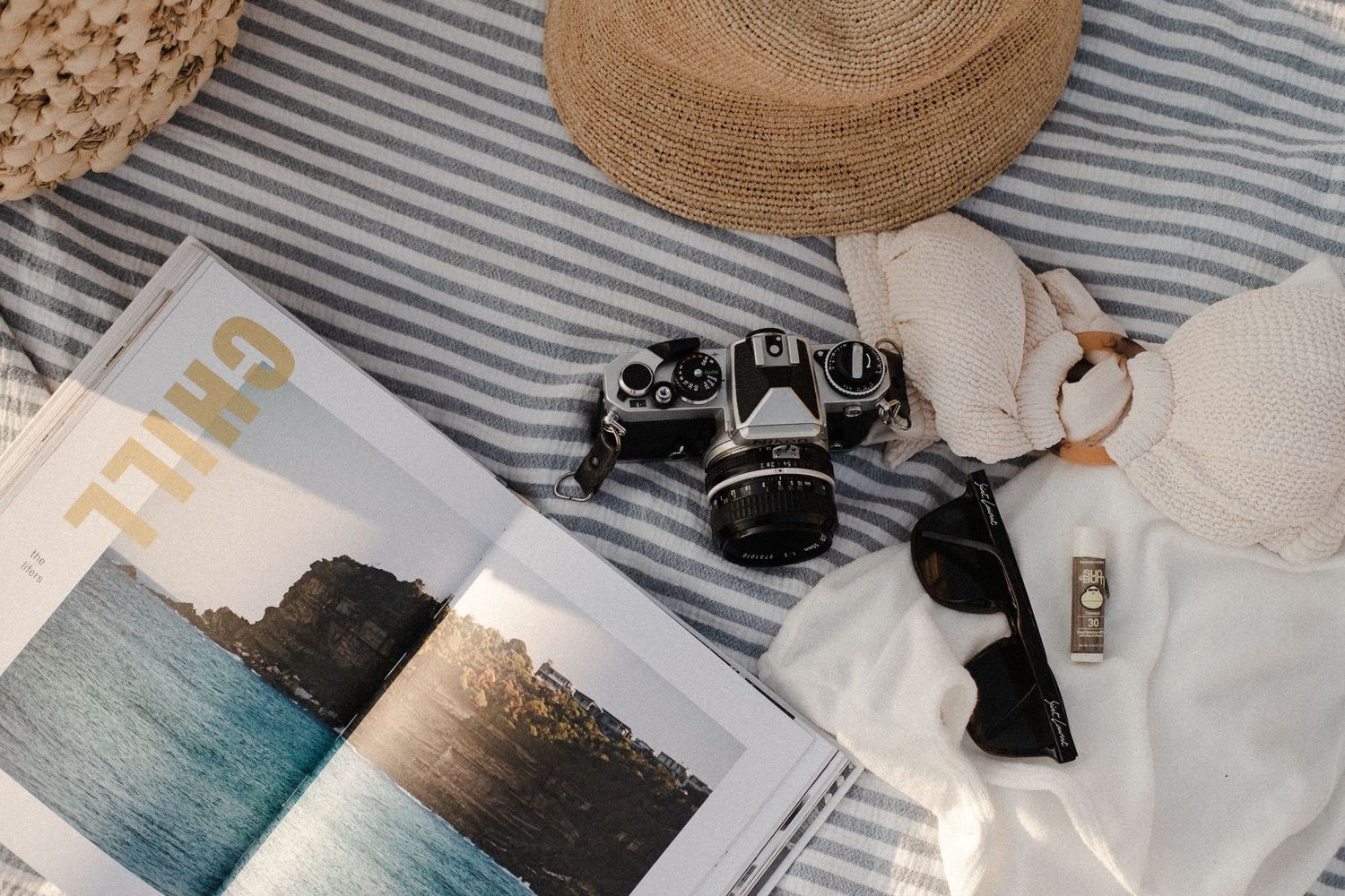 A lifestyle flat lay with camera equipment, straw hat, and striped textiles.