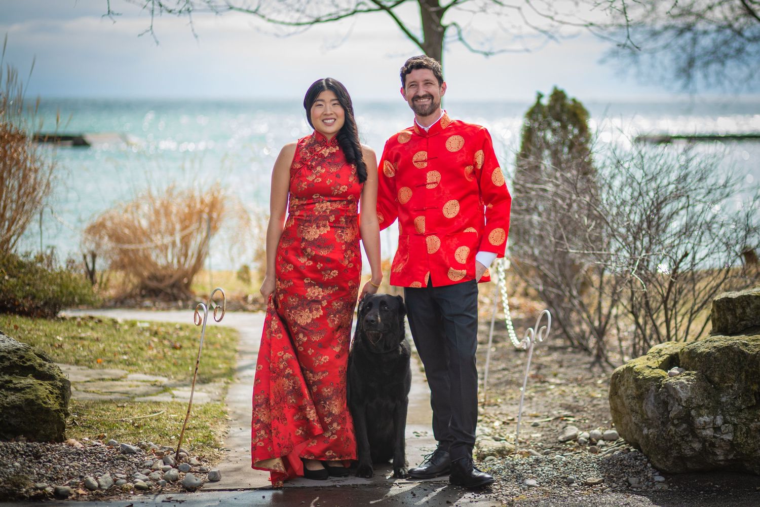 A couple in matching red traditional attire stands together on a coastal path.