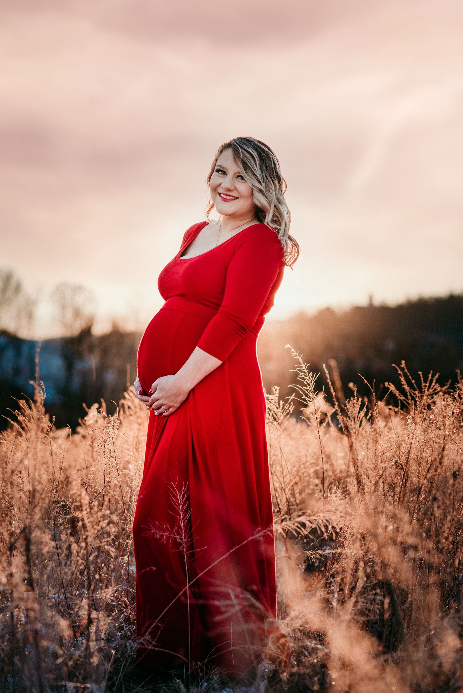 pregnant woman poses in a red dress in a field at sunset | west virginia maternity photographer