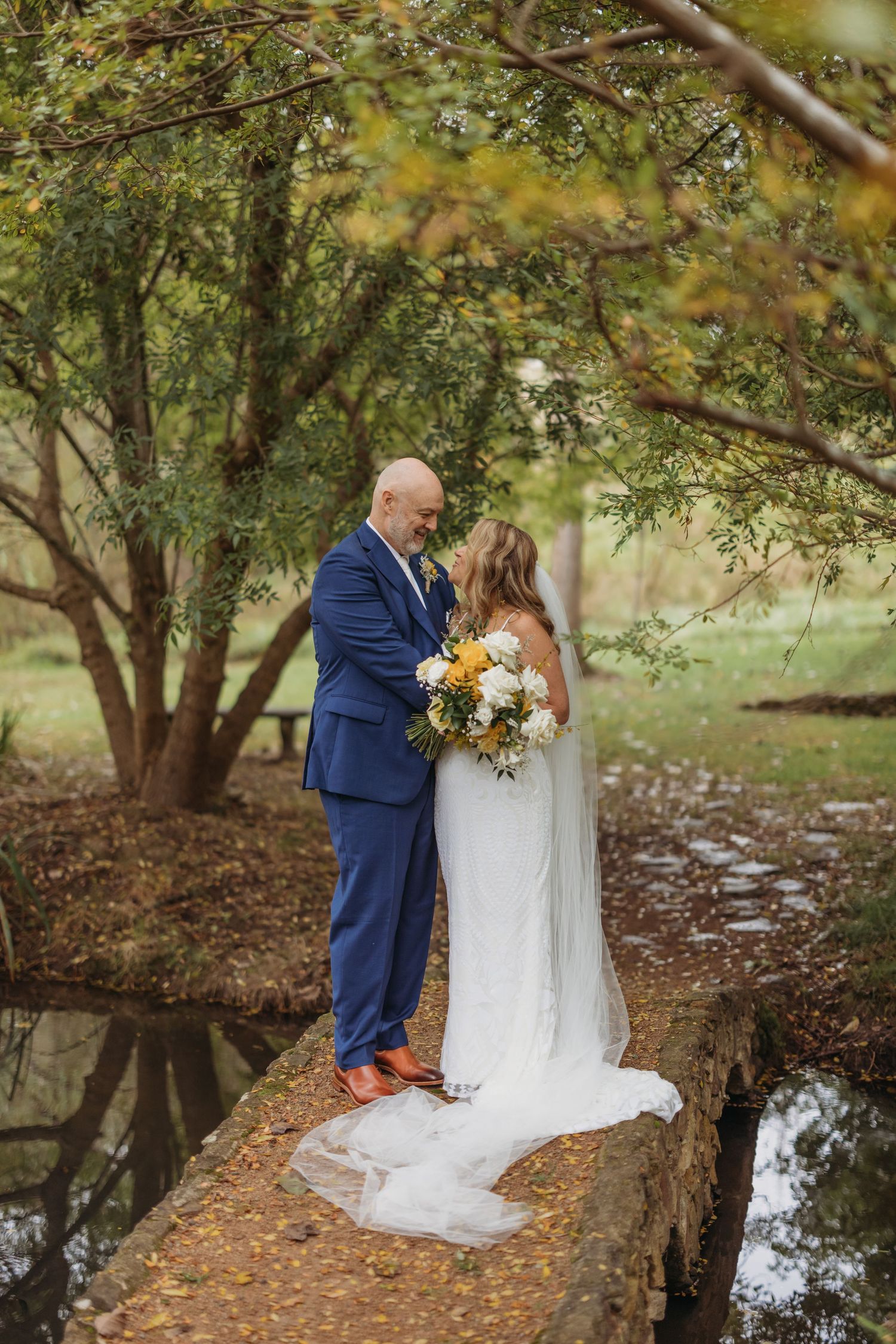 Couple shares intimate moment on stone bridge in romantic garden setting.