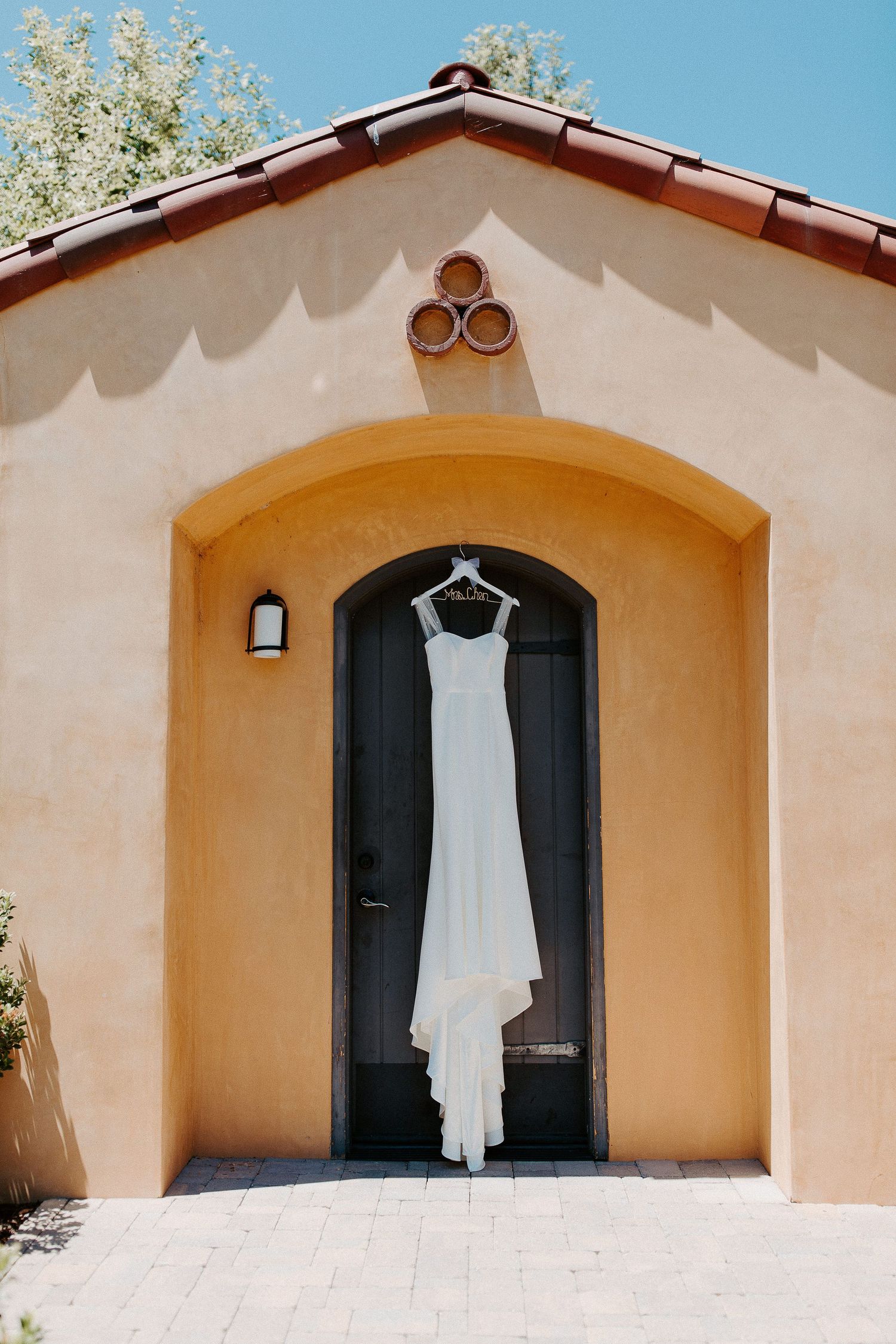 White wedding dress hanging on black door of Mediterranean style building with peach walls.