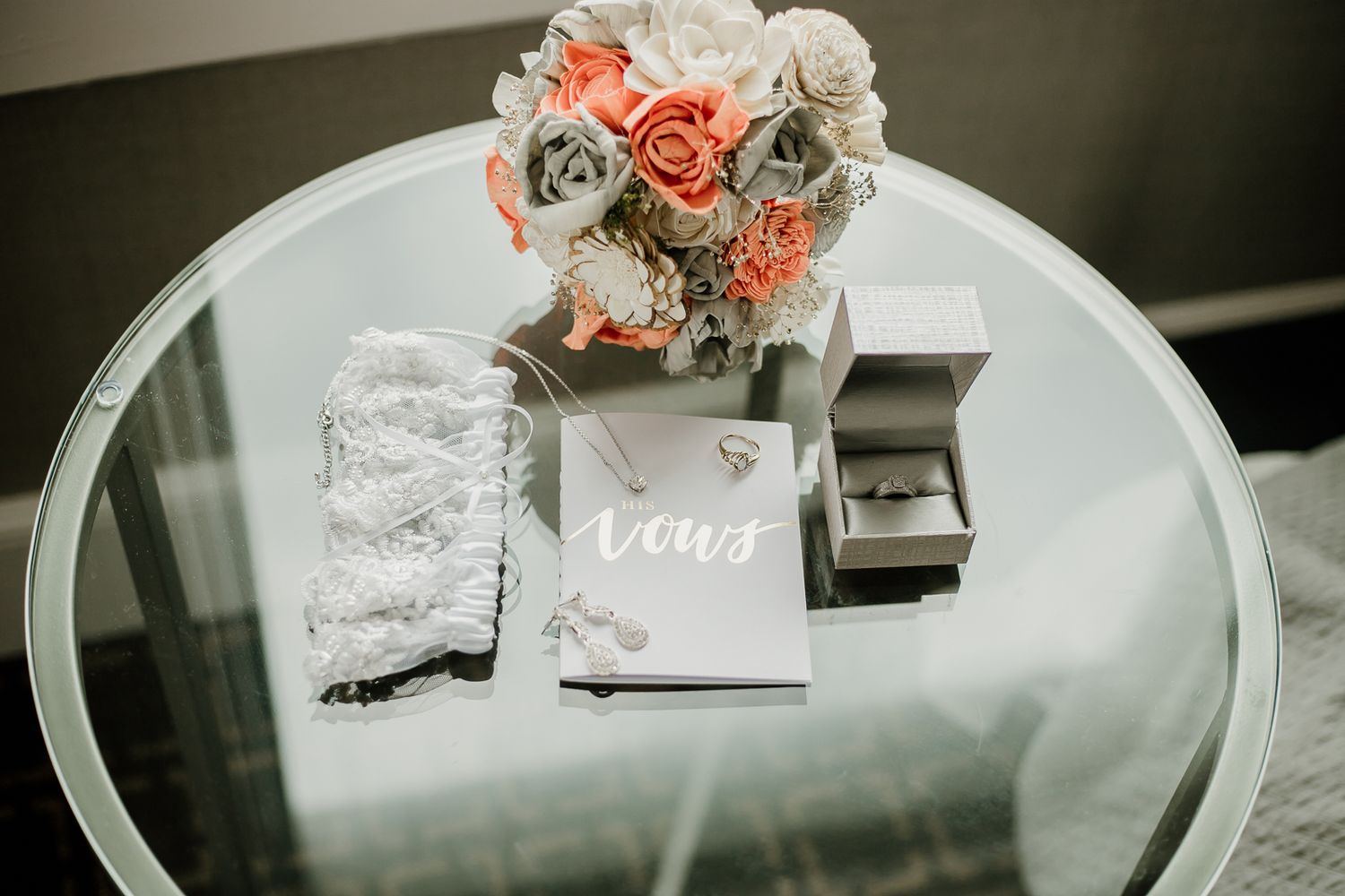 Wedding details featuring coral and white roses arranged on reflective surface.